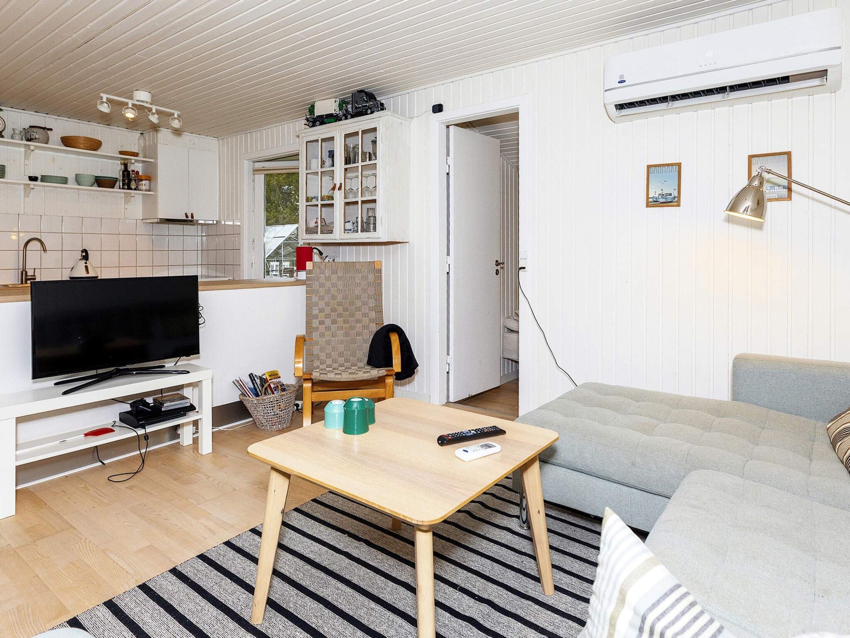 A compact living space with a television, a dining table, a sofa, and a kitchen area.