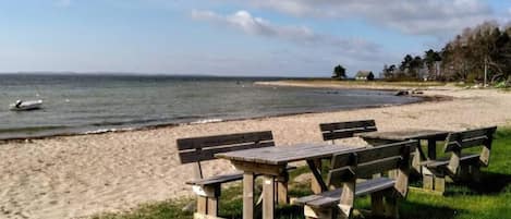 A beach with wooden picnic tables and a boat in the water.