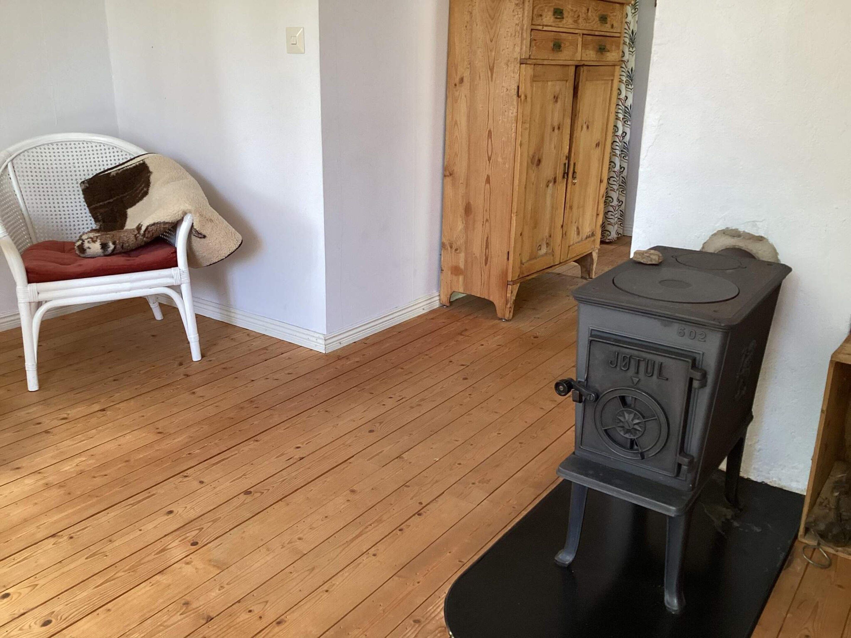 Ein Zimmer mit einem weißen Stuhl, einem Holzschrank und einem schwarzen Herd.