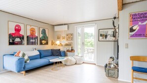 A cozy living room with a blue sofa, a small coffee table, and a wooden chair. There are framed pictures on the walls and a window with a view of the outdoors. - 6 Person Holiday Home in Henne (Henne)