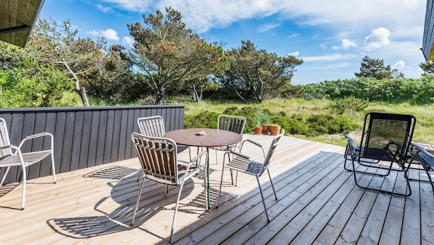 A wooden deck with a round table and four chairs, surrounded by greenery and trees. - 6 Person Holiday Home in Henne (Henne)
