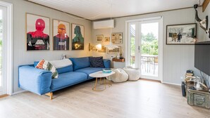 A modern living room with a blue sofa, a small round table, and a fireplace. There are framed pictures on the walls and a window overlooking a garden. - 6 Person Holiday Home in Henne (Henne)