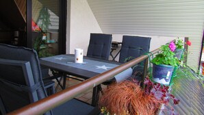 Eine Terrasse im Freien mit Tisch, Stühlen, einer weißen Tasse und Topfpflanzen.
