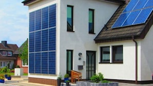 Ein modernes, zweistöckiges Haus mit großen Solaranlagen auf dem Dach und einer geräumigen Auffahrt.