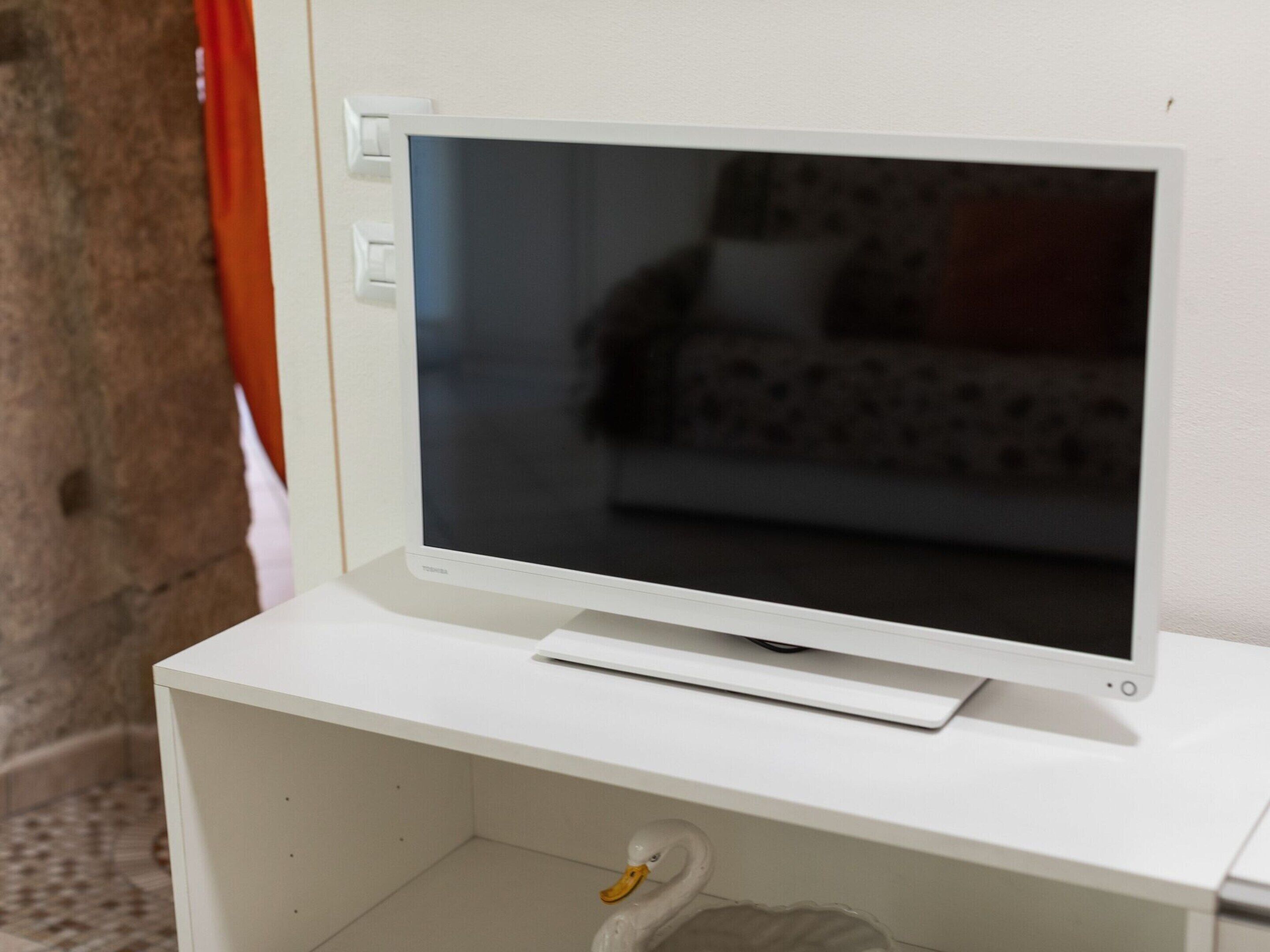Een witte tv-meubel met een flatscreen televisie, een afstandsbediening en een decoratief zwaanbeeldje.