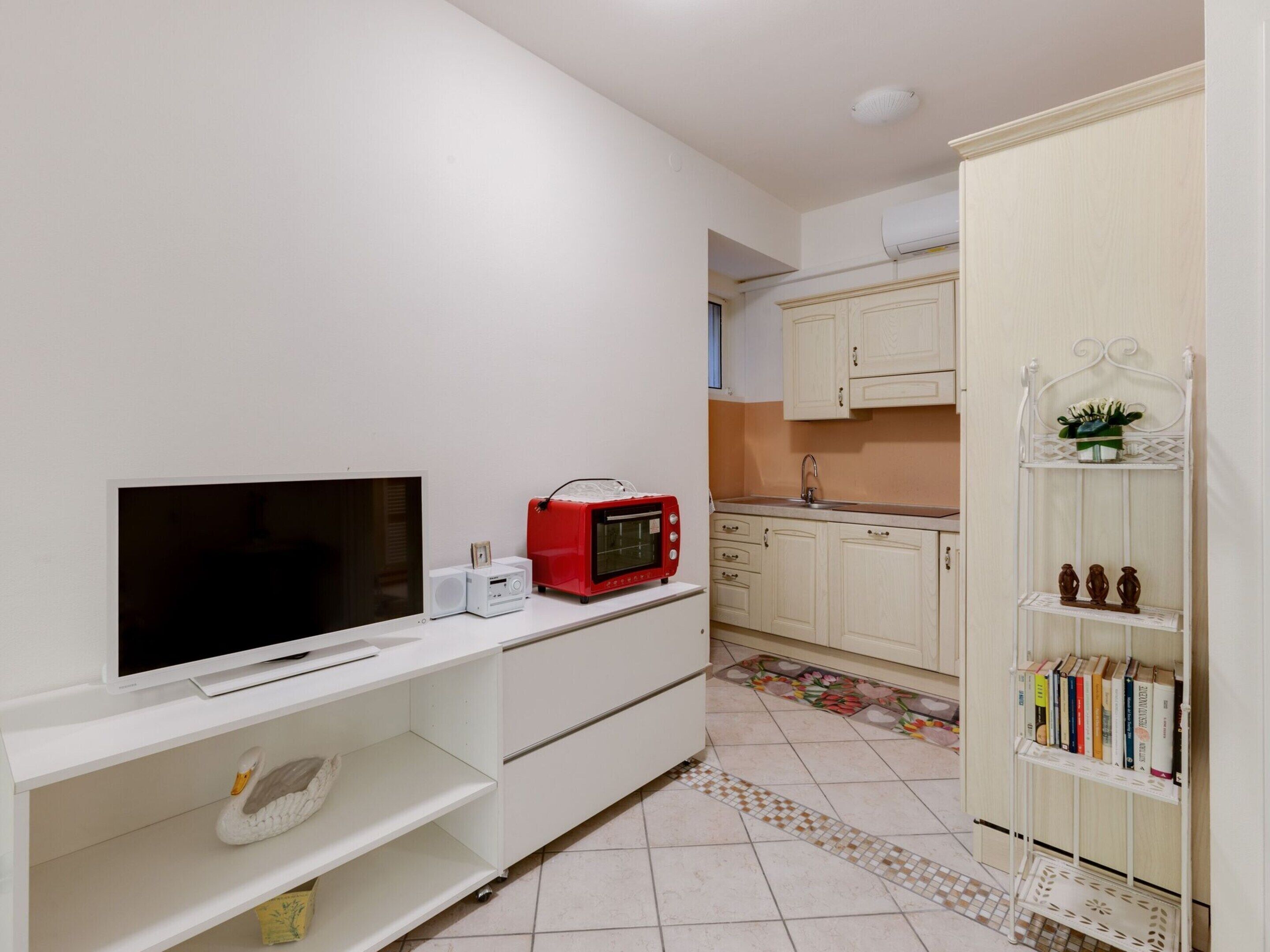 A compact kitchen with white cabinets, a red microwave, a white toaster, and a TV on a white shelf.