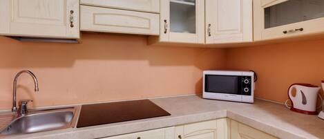 A kitchen with light wooden cabinets, a stainless steel sink, a microwave, and a kettle.