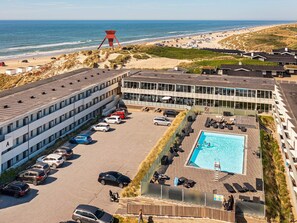 A hotel with a swimming pool, parking lot, and beach view.