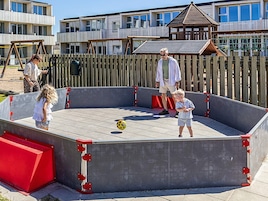 A children's play area with a concrete structure, a wooden fence, and a building in the background.