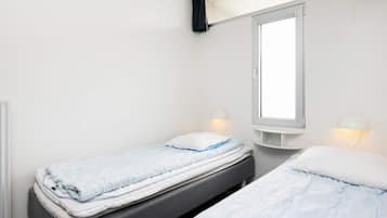 Una habitación pequeña y limpia con dos camas individuales, una ventana con cortinas y lámparas de lectura en la pared.