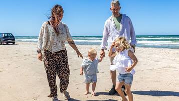 Una familia caminando sobre una playa arenosa, con el océano al fondo.