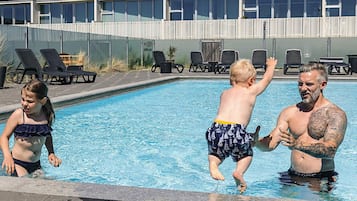 Una piscina con sillones de descanso y un edificio al fondo.