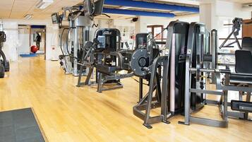 Un gimnasio con diversas máquinas de ejercicio, suelo de madera y una pared azul de fondo.
