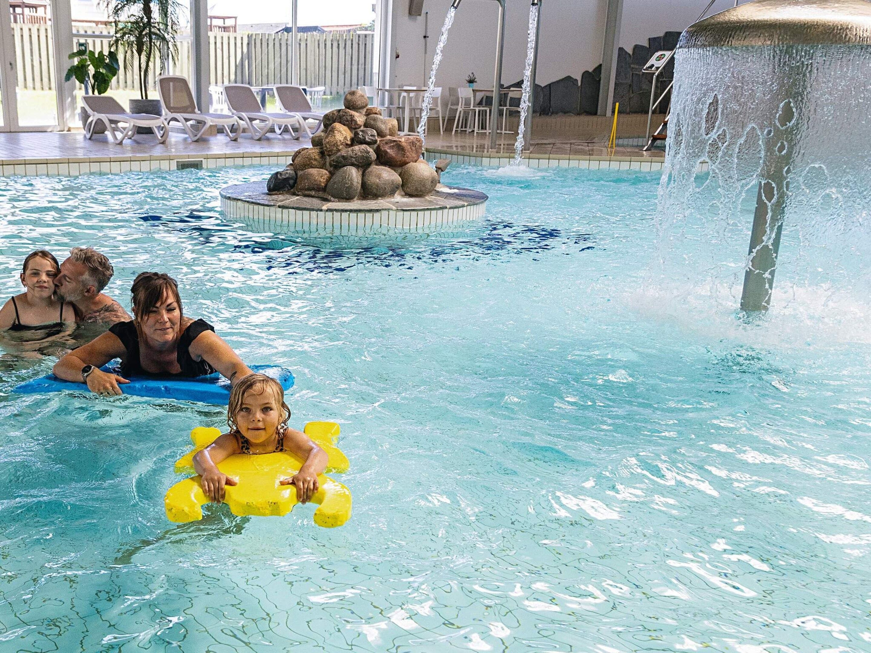 A pool with a water fountain, lounge chairs, and a rock feature.