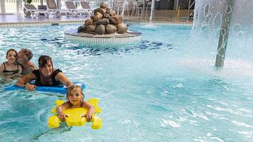 A pool with a water fountain, lounge chairs, and a rock feature.