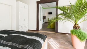 A bedroom with a bed, a large mirror, a potted plant, and a view into the kitchen area. - Holiday Apartment Angela Koenig (Wernigerode)