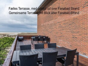 Une terrasse extérieure avec un mur en briques, une plateforme en bois et des meubles en osier.