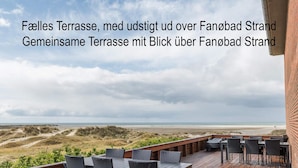Een houten terras met buitenmeubilair met uitzicht op een strand en duinen.