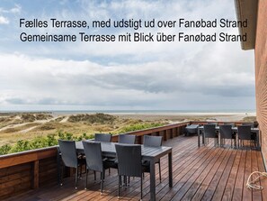 Eine Holzterrasse mit Gartenmöbeln mit Blick auf Strand und Dünen.