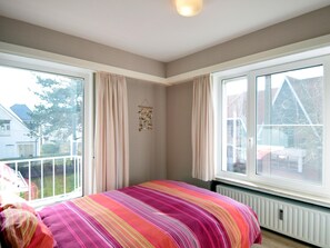 Ein Schlafzimmer mit großem Fenster, einem Bett mit farbenfroher Streifenauflage und einem Heizkörper unter dem Fenster.