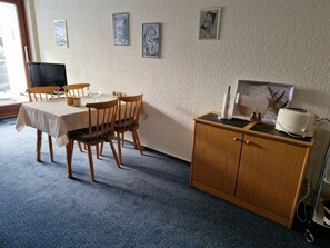 A dining area with a table set for four, wooden chairs, a small cabinet with a toaster, and a television on a stand.