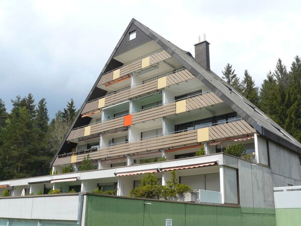 A multi-story building with a sloped roof, balconies, and a chimney.