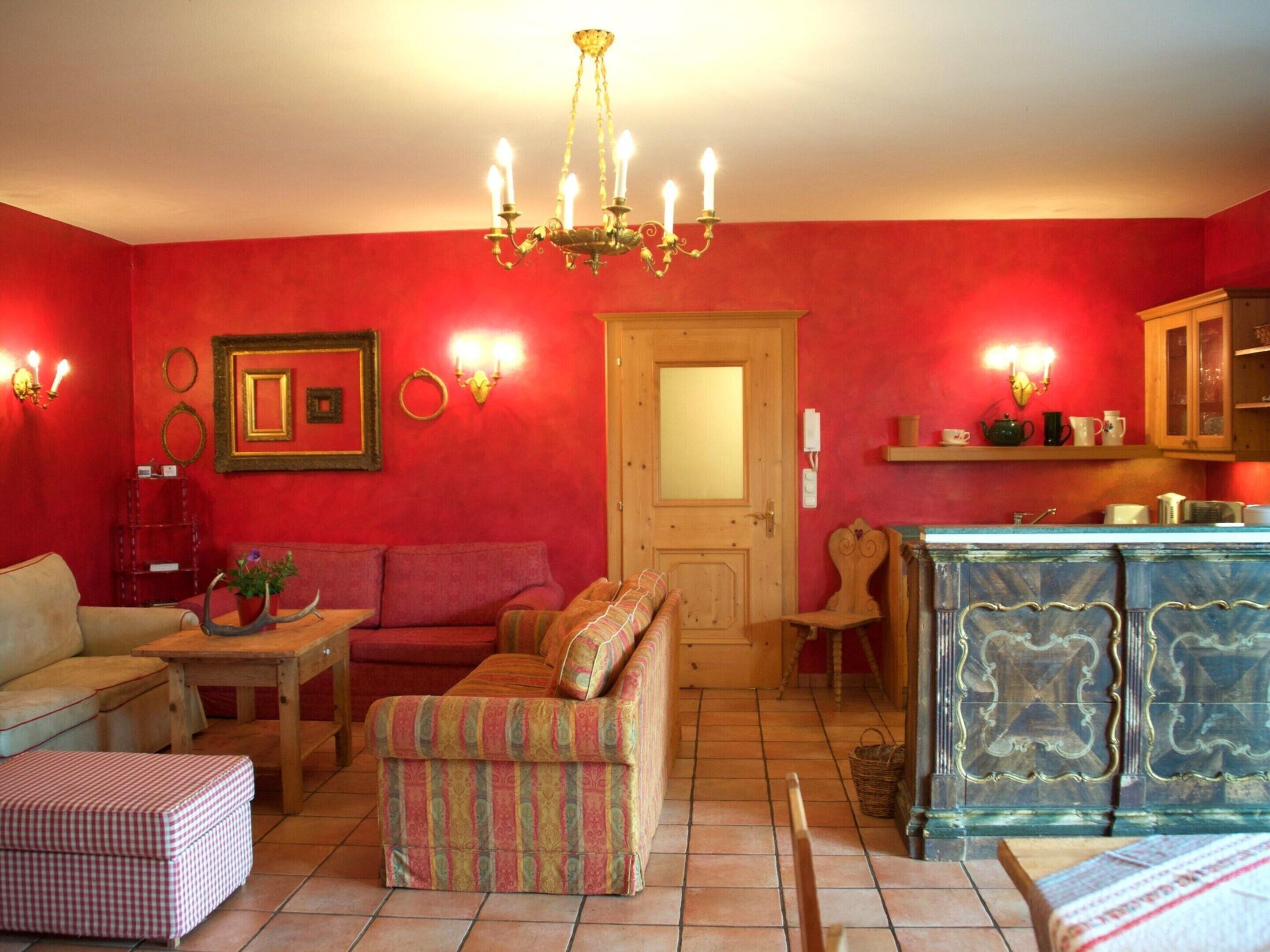 A cozy living room with a red wall, a wooden door, a sofa, a small table, and a cabinet.
