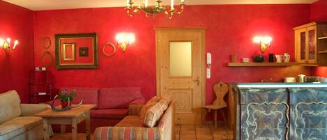 A cozy living room with a red wall, a wooden door, a sofa, a small table, and a cabinet.