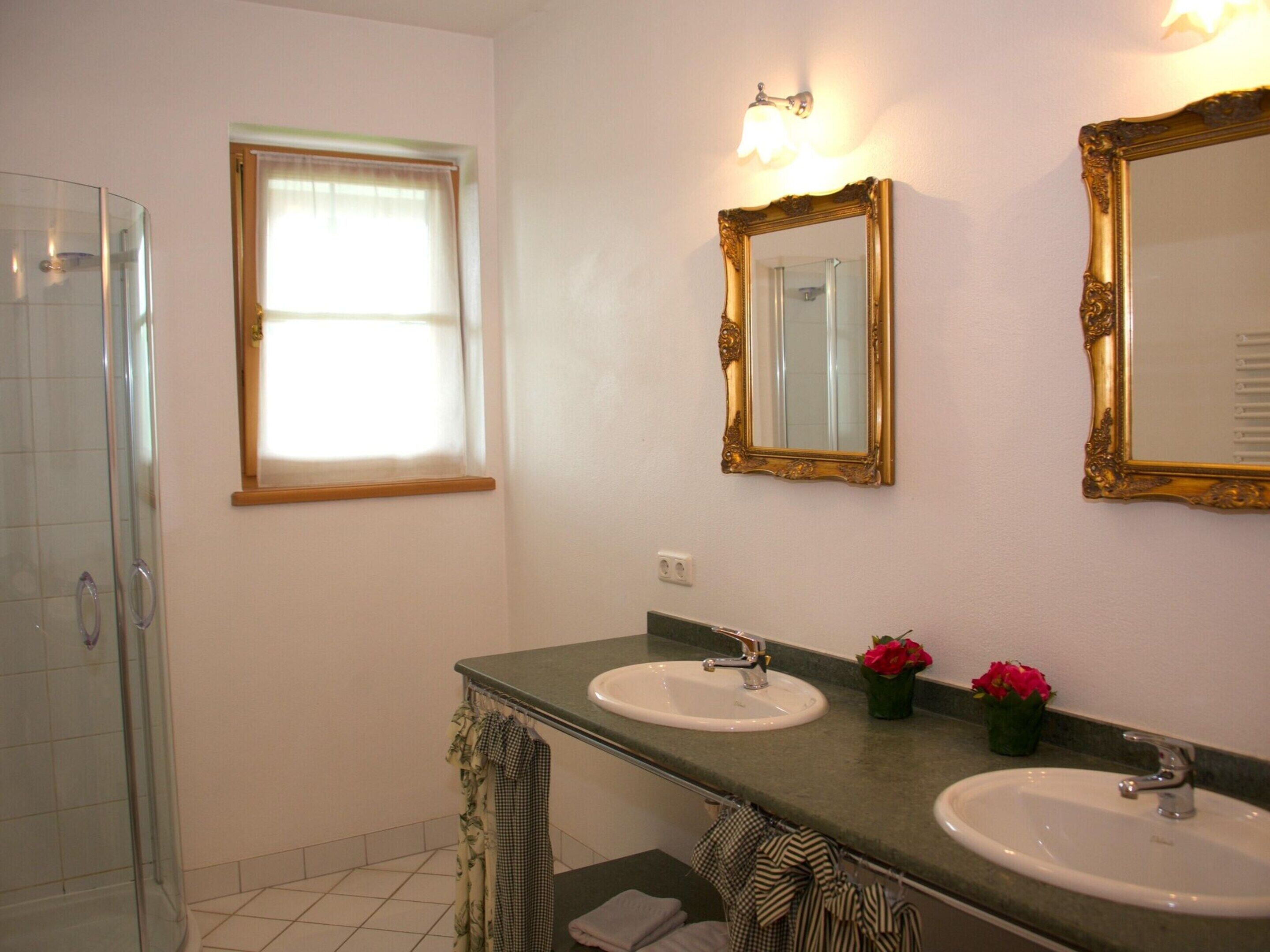 A bathroom with two sinks, a shower, and two mirrors with ornate frames.