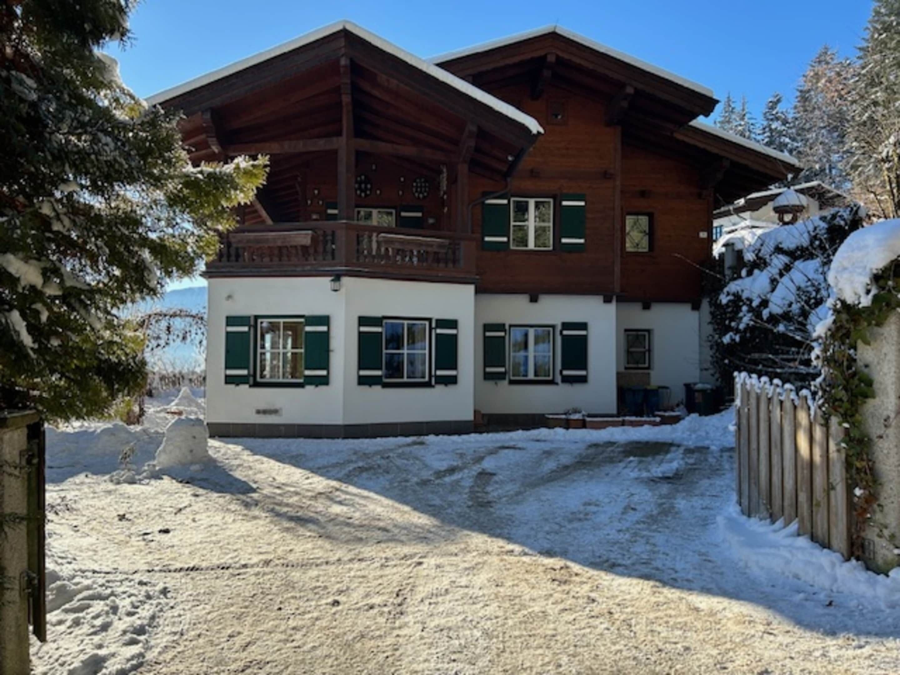 En tvåvånings chalet i trä med en balkong, snötäckt omgivning och en klar himmel.