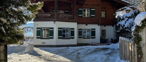 En tvåvånings chalet i trä med en balkong, snötäckt omgivning och en klar himmel.