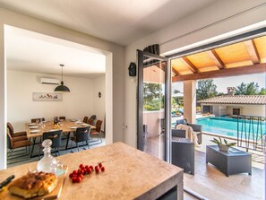 A dining area with a table set for four, a kitchen area, and a view of a swimming pool and outdoor seating.