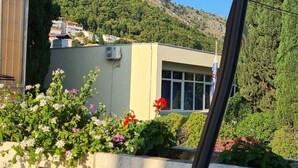 A building with a beige facade, a window, and a flag. There are flowers in front of the building. - Apartment Solvit - Three Bedroom Apartment With Terrace (Dubrovnik)