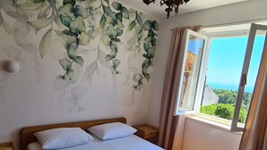 A bedroom with a bed, a nightstand, a window with curtains, and a view of greenery outside. - Apartment Solvit - Three Bedroom Apartment With Terrace (Dubrovnik)