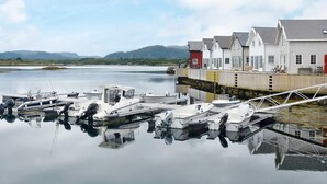 A marina with several boats docked, a row of houses with a red section, and calm water reflecting the boats and houses. - 6 Person Holiday Home in Bud (Averoy)
