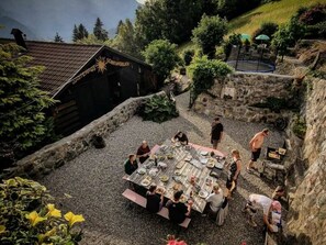 An outdoor dining area with a stone wall, a wooden table, and a grill.