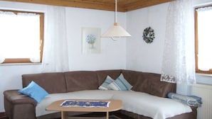 A cozy living room with a brown sofa, a small wooden table, and a hanging lamp. - Haus Nett Modern Retreat (Stiefenhofen)