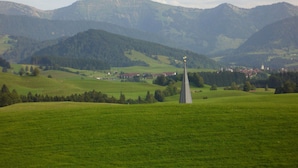 A rural landscape with a church steeple in the foreground, surrounded by rolling hills and a small village in the distance. - Haus Nett Modern Retreat (Stiefenhofen)