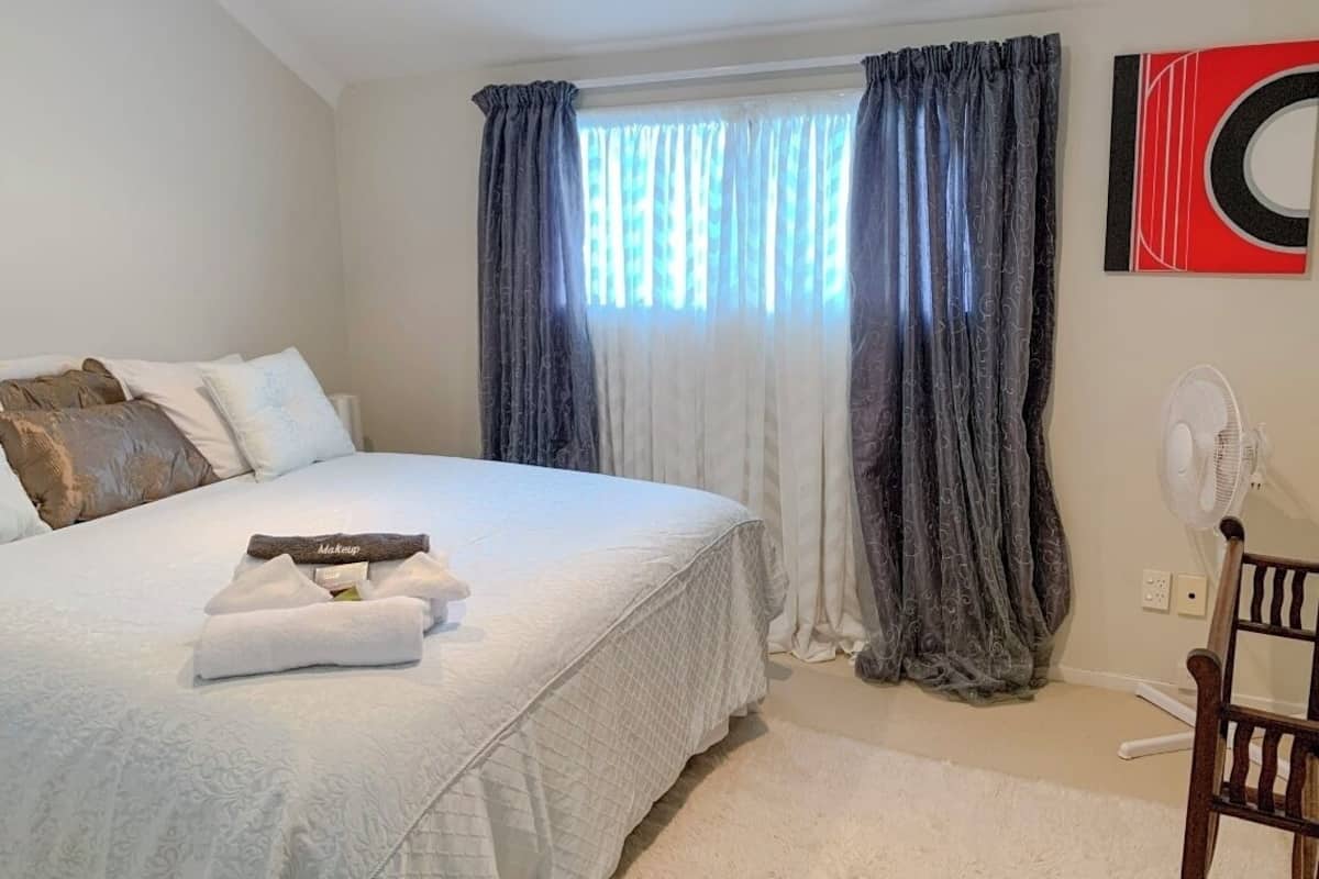 Un dormitorio con una cama grande, una mesita de noche, una silla y una ventana con cortinas.