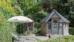A wooden cabin with a small porch, a covered seating area with a white umbrella, and a poolside lounge with two chairs. - Krahenberg Country House (Eslohe)