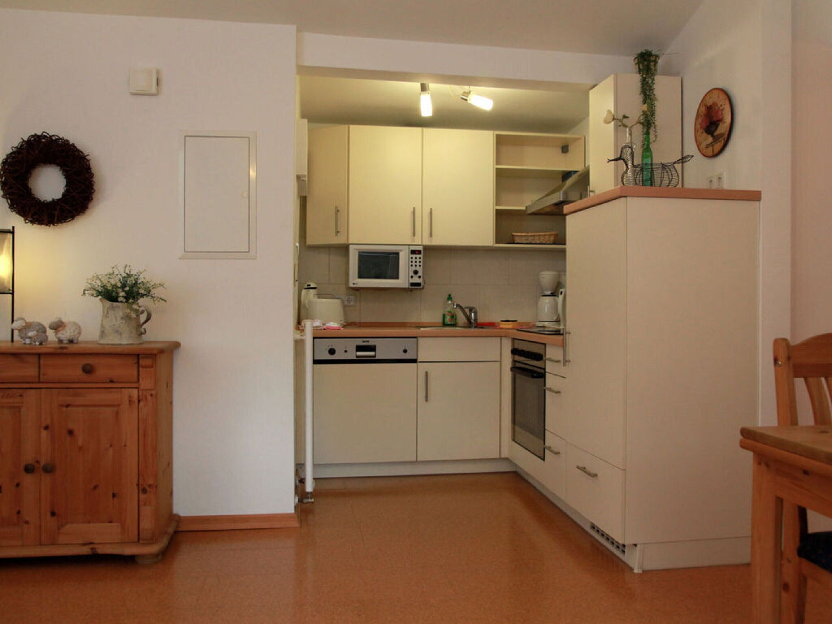 A compact kitchen with white cabinets, a microwave, a dishwasher, and a wooden cabinet with decorative items.