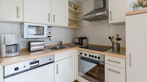 A modern kitchen with white cabinets, a microwave, toaster, sink, stove, and a coffee maker. - Krahenberg Country House (Eslohe)