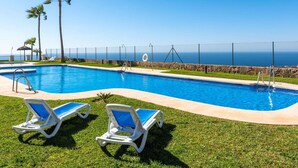 A swimming pool with two lounge chairs, a stone wall, and a view of the ocean. - Belvilla by OYO La Zenaida II (Rincon de la Victoria)
