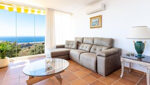 A living room with a large window, a sofa, a glass coffee table, and a lamp. - Belvilla by OYO La Zenaida II (Rincon de la Victoria)
