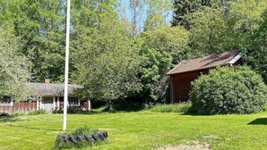 A grassy yard with a wooden fence, a small building with a tiled roof, and dense trees in the background. - 4 Person Holiday Home in Anneby (Aneby)
