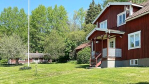 A two-story wooden house with a balcony, surrounded by a grassy yard and trees. - 4 Person Holiday Home in Anneby (Aneby)