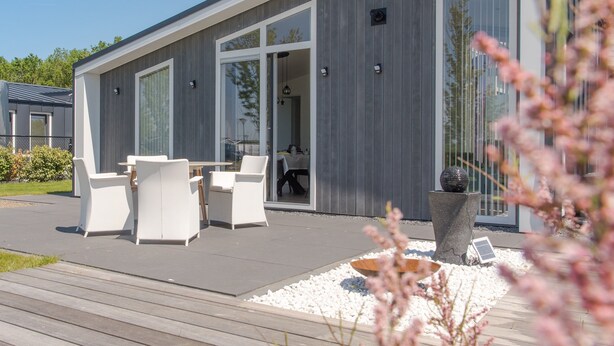 Ein modernes Haus mit einer Terrasse, weißer Möbel und einem großen Fenster.