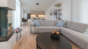 Ein modernes Wohnzimmer mit einem grauen Ecksofa, einem schwarzen Couchtisch und einem Kamin aus Glas.