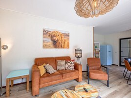 Un salon avec un canapé marron, une table basse en bois, un réfrigérateur bleu et un luminaire suspendu en osier.