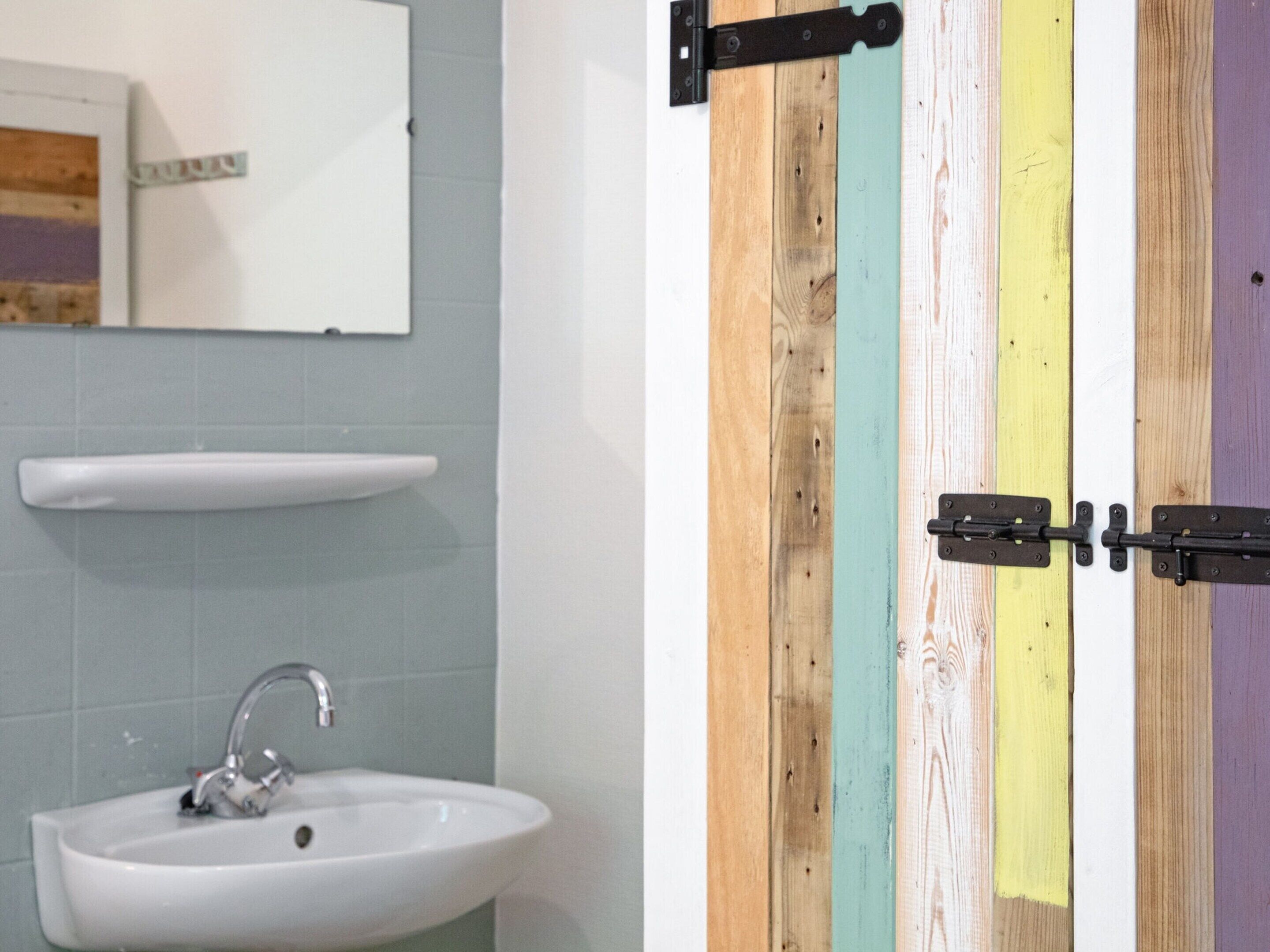 A bathroom with a white sink, a mirror, and a door with a wooden panel design.